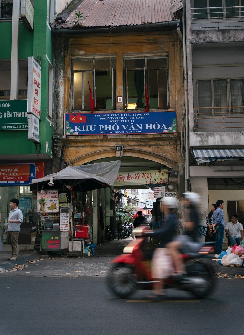 A red motorbike blurred by motion passing a street stall in front of an old building in Ho Chi Minh City
